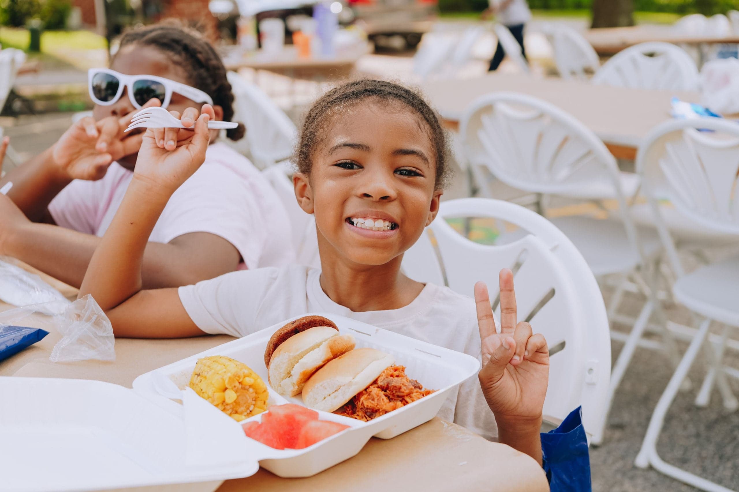 Young girl smiles and gives a peace sign while enjoying a hot meal