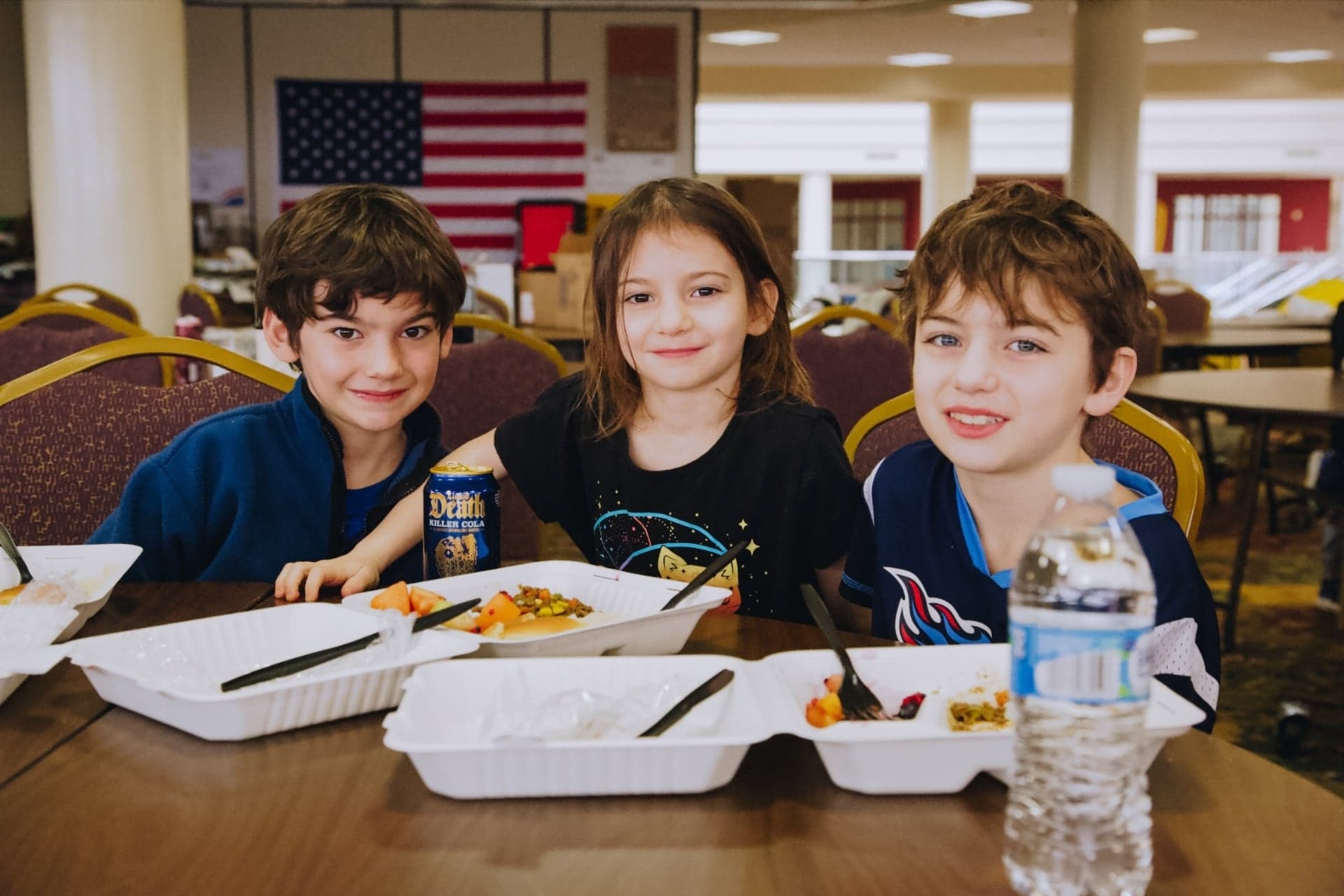 Three children smile as they eat hot meals