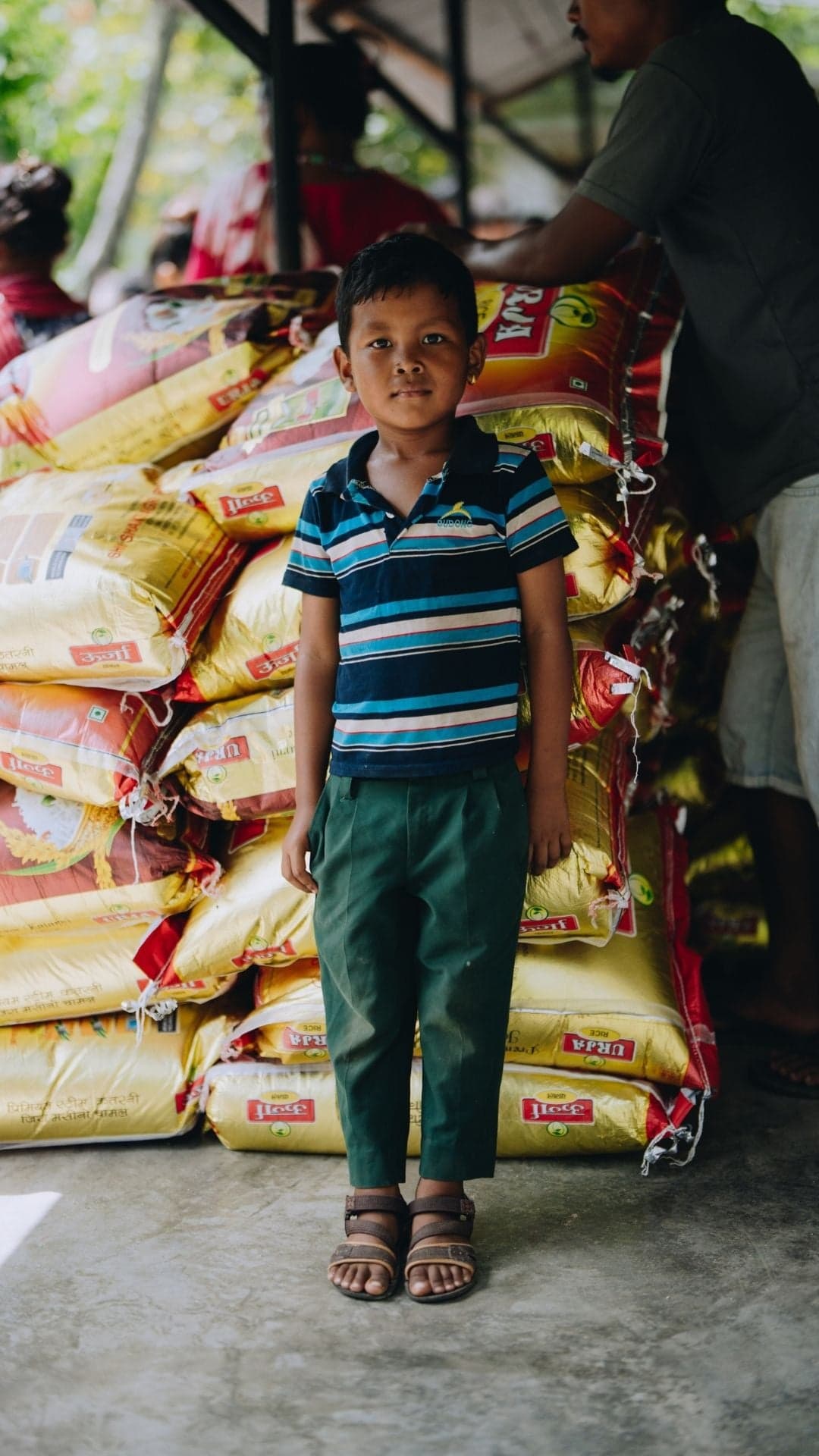 A boy in Nepal stand next packs of rice.