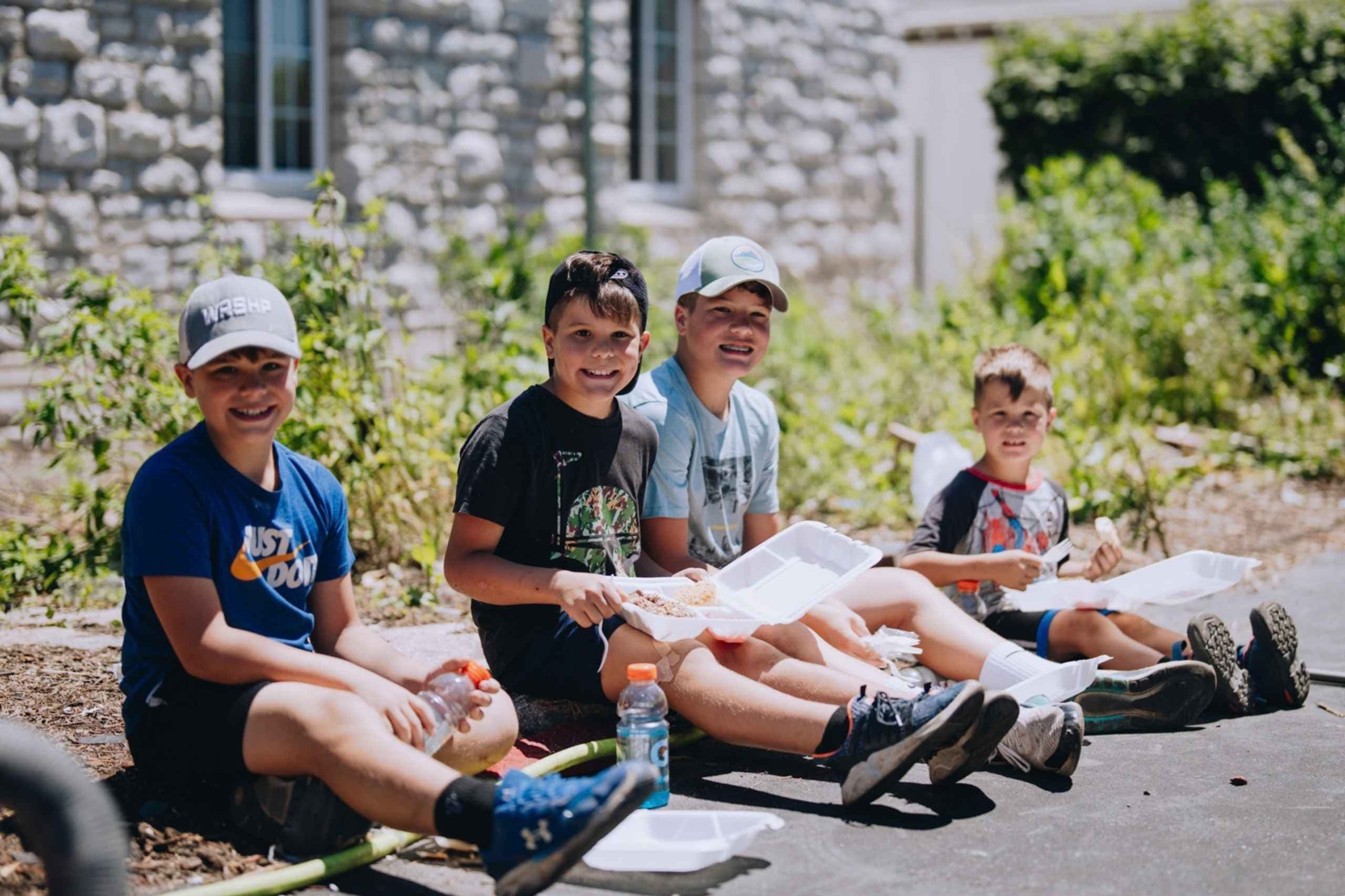 Group of boys smiling as the sit on the street and eat hot meals