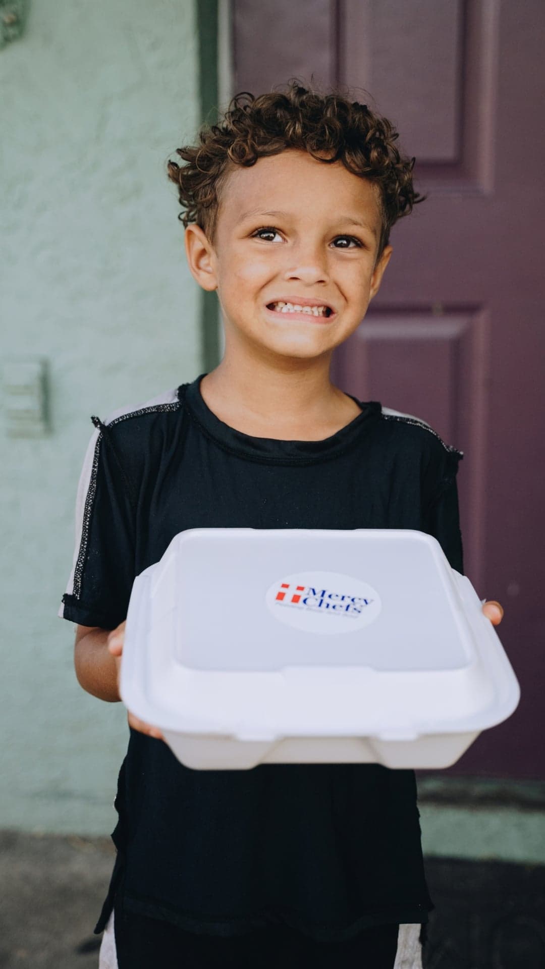 Young boy smiles as he holds a Mercy Chefs meal