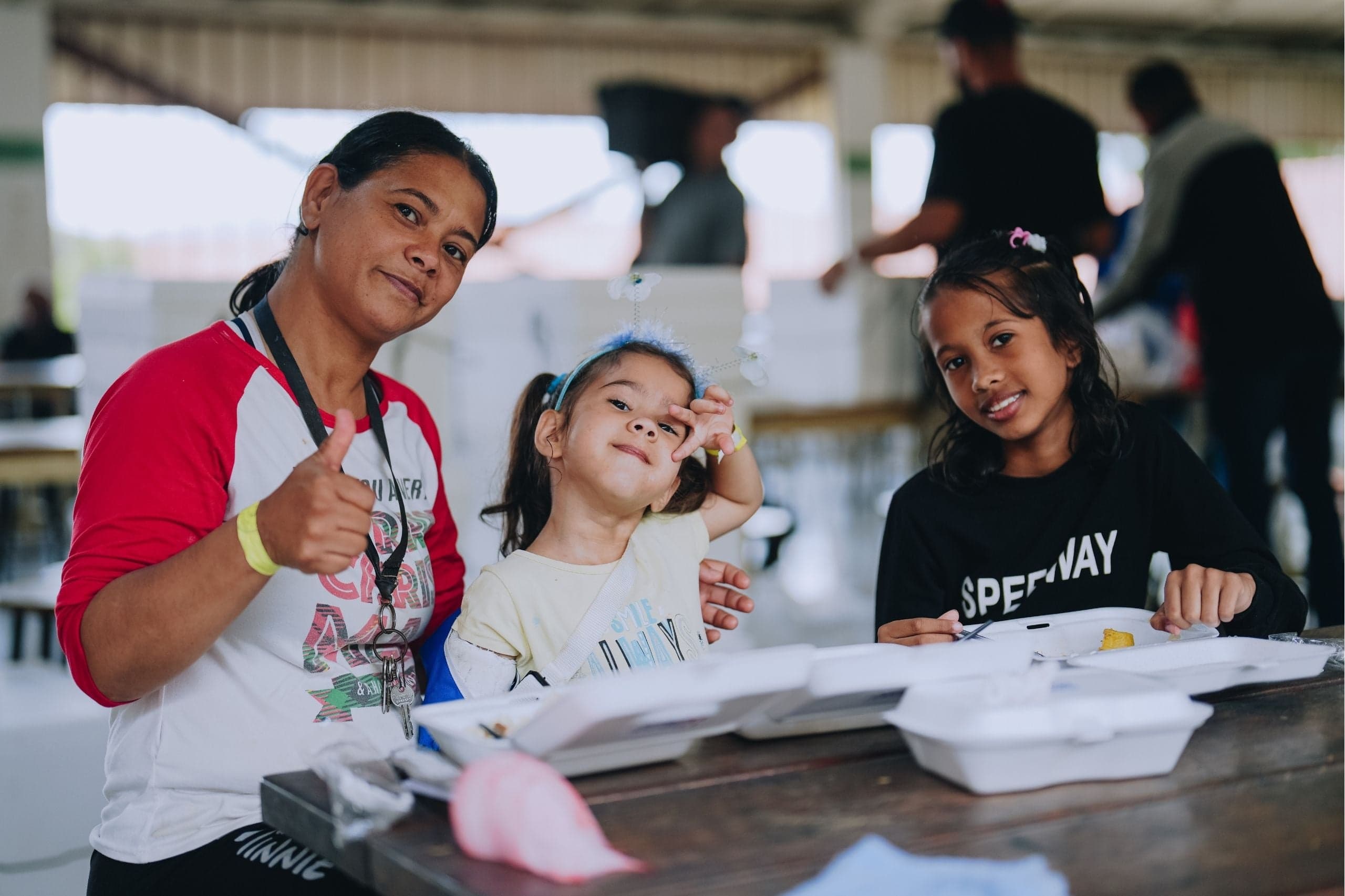 A mother and her daughters give a thumbs-up as they eat Mercy Chefs meals in Venezuela.