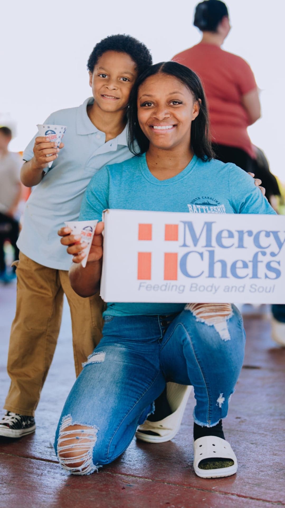 A mother and son smile as the mother holds a Family Grocery Box.