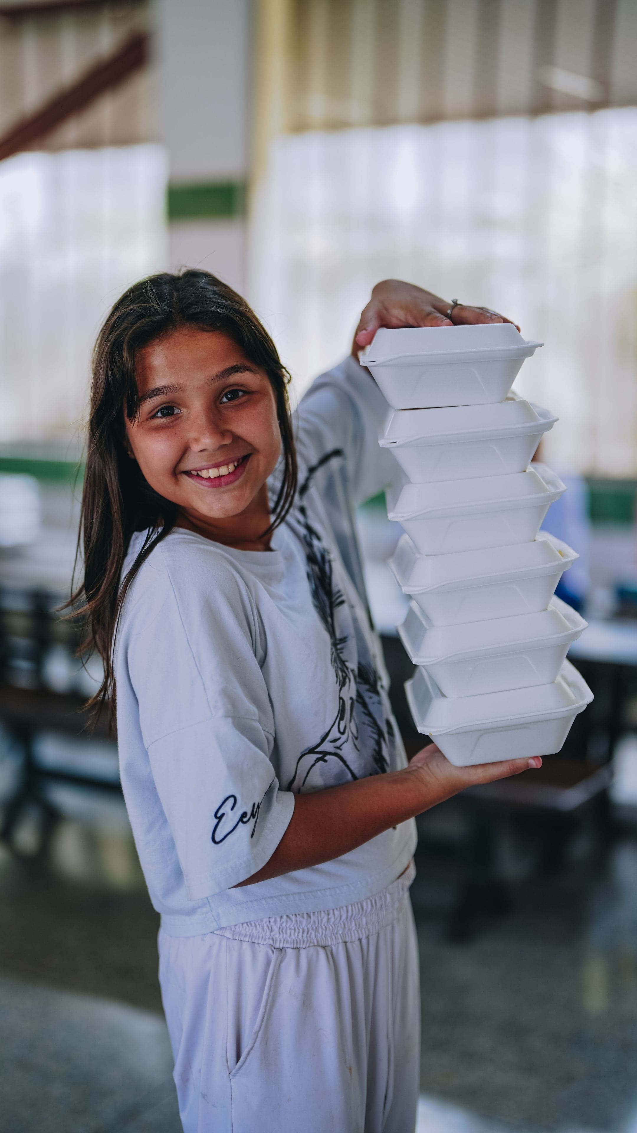 A young girl in Venezuela holds hot meals with a smile.