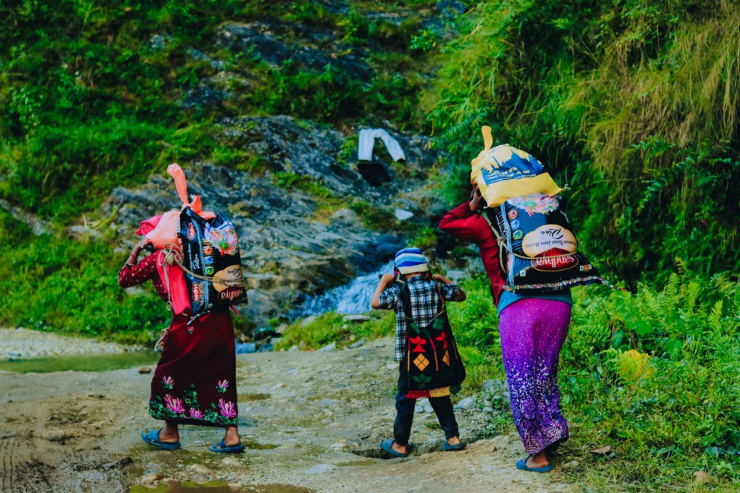 Two women and a boy carry groceries up a hill in Nepal